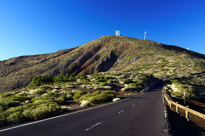 Road leading towards green mountain against clear blue sky