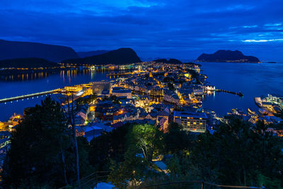 High angle view of illuminated city by sea against sky