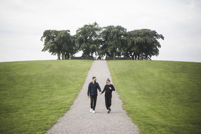 Smiling couple walking amidst grassy field against trees and sky