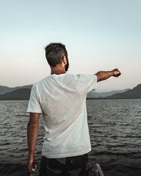 Rear view of man pointing while standing against clear sky