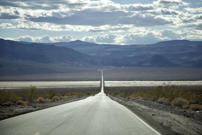 Road leading towards mountains against sky