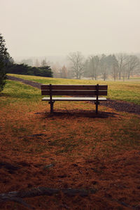 Empty bench on field against sky