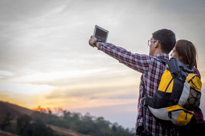 Low angle view of man photographing on mobile phone against sky