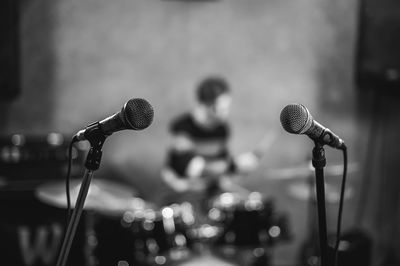 Microphones on stands with musician playing drum kit in background
