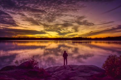 Silhouette man standing on lake against sky during sunset