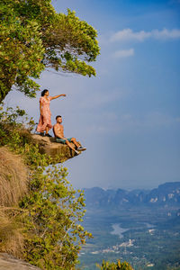 People sitting on tree by mountain against sky