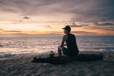 Rear view of man standing at beach against sky during sunset