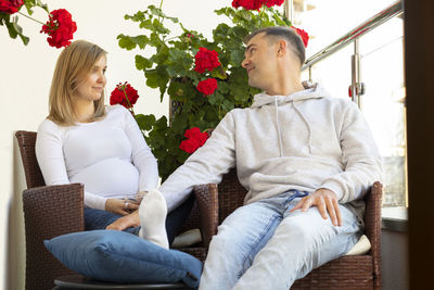 White caucasian pregnant woman and her husband rest on terrace, balcony of new campus,sit in chair