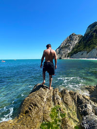 Full length of shirtless man looking at sea against clear sky