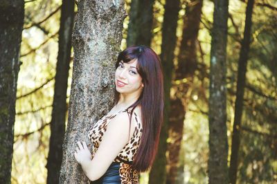 Side view of beautiful young woman standing on tree trunk