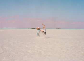 Playful couple at beach against sky