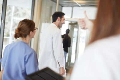 Cropped image of female nurse showing thumbs up to young doctor walking with coworker in lobby at hospital