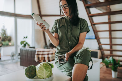 Full length of woman holding mobile phone at home