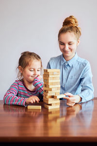 Little girl preschooler and her elder sister playing together with wooden blocks game toy