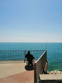 Bicycle on railing by sea against clear sky