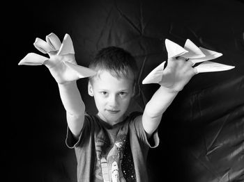 Portrait of boy holding paper while standing against black background