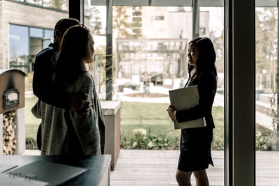 Customers talking with saleswoman standing by window in kitchen at home