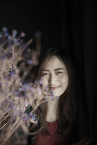 Portrait of beautiful young woman by flowers against curtain at home
