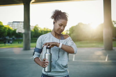 Woman checking time on smart watch while holding water bottle on street