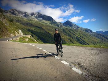 Man riding bicycle on road against mountain range during sunny day