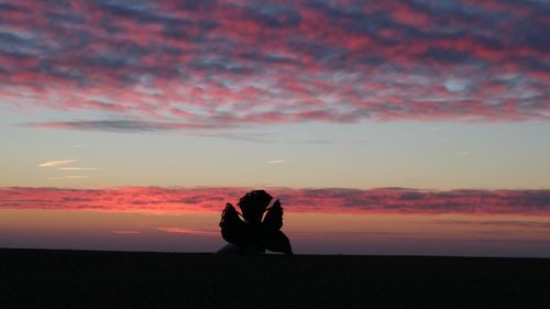 Silhouette men sitting against sky during sunset