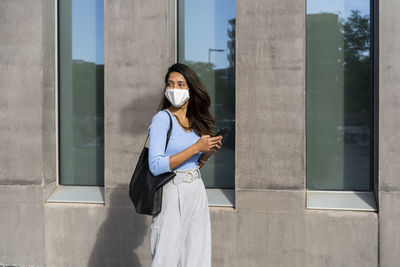 Young woman using phone while standing on wall