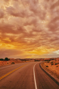 Golden sunset over storm clouds along empty highway in moab, utah.
