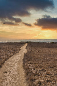 Dirt road on field against sky during sunset