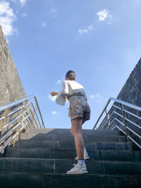 Low angle view of woman standing on staircase against sky