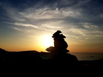 Silhouette man standing on rock by sea against sky during sunset