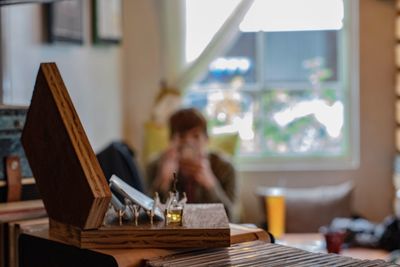 Close-up of objects on table with person sitting in background at home