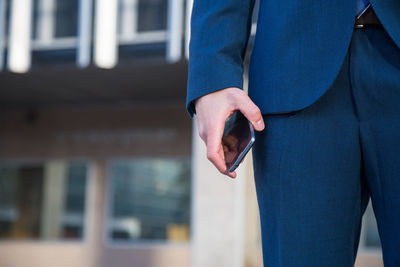 Midsection of businessman holding mobile phone while standing in city