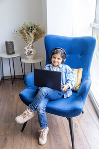 High angle portrait of girl using laptop while sitting on chair