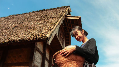 Low angle view of woman smiling and holding traditional  bucket in front of local asian hut