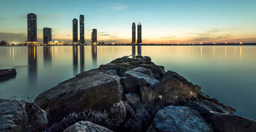 Scenic view of sea and skyscrapers against sky at sunset