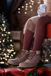 Low section of woman sitting on illuminated christmas tree