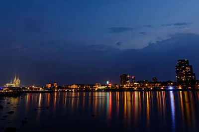 Illuminated buildings by sea against sky at night