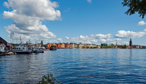 Sailboats moored on sea by buildings against sky