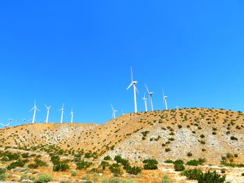 Wind turbines on land against clear blue sky