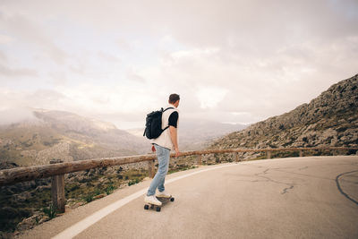 Man with backpack skateboarding on road near mountains against sky
