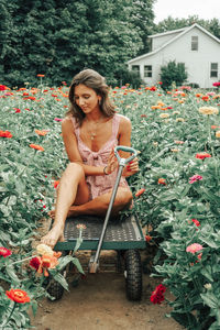 Young woman sitting on cart amidst flowers blooming in yard