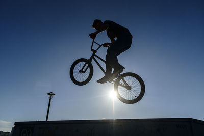 Low angle view of man doing stunt with bicycle against clear sky