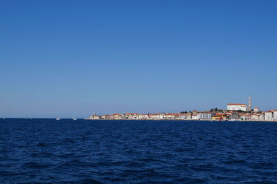 Sea by buildings against clear blue sky