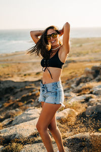 Woman wearing sunglasses while standing at beach during sunset