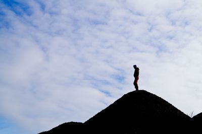 Low angle view of man standing on hill against cloudy sky