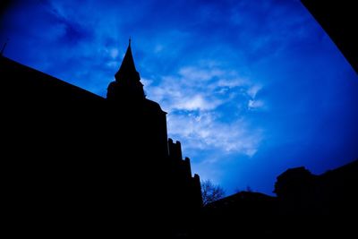 Low angle view of silhouette building against blue sky