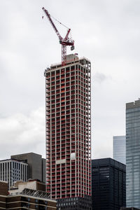 Low angle view of crane by buildings against sky