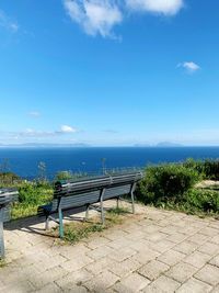 Empty bench by sea against blue sky