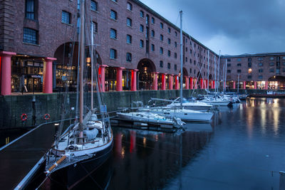 Boats moored in canal by buildings at dusk