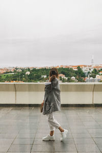 Rear view of woman walking on tiled floor against sky